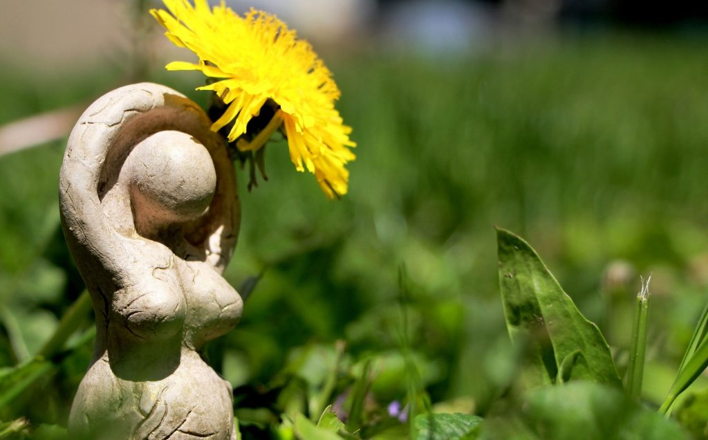 Mutter Natur Statue steht neben Löwenzahnblüte: Hello World!