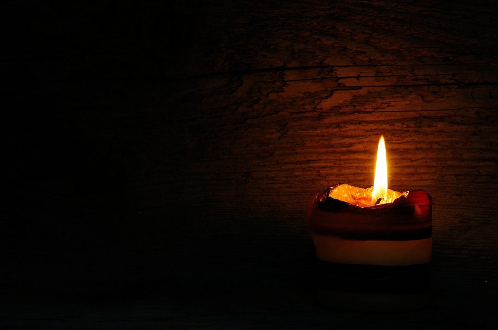 Brennende Kerze vor einer dunklen Holzwand. Ob sie für Imbolc angezündet wurde?